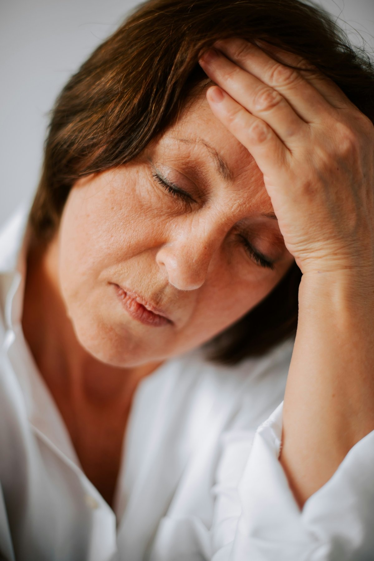 Middle-aged woman with closed eyes and hand on forehead, appearing fatigued from perimenopause, preparing to seek support through nutrition counseling covered by insurance to improve energy and hormonal balance.